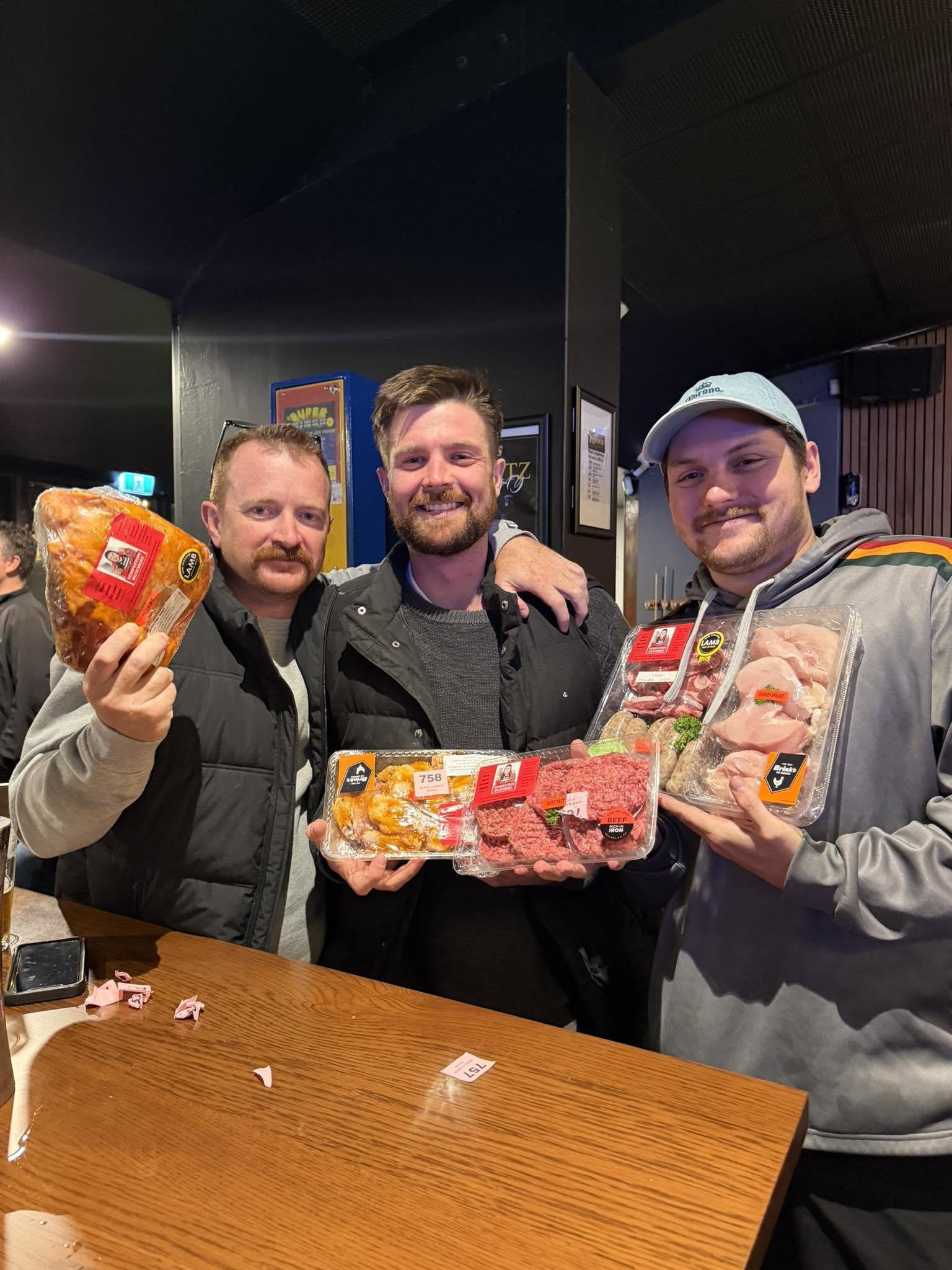 Three friends showing off their meat raffle prizes
