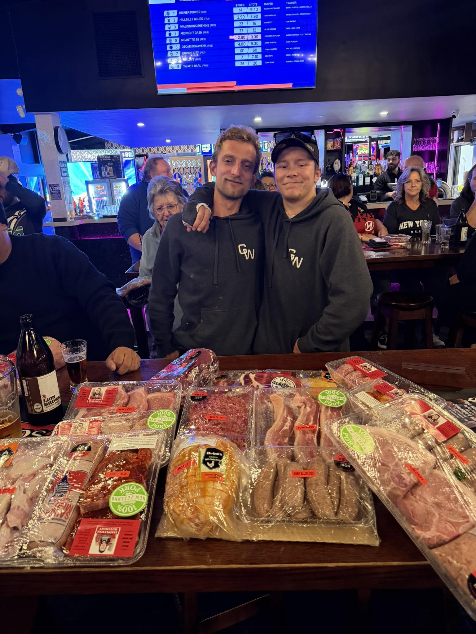 Two patrons behind a table full of meat raffle prizes