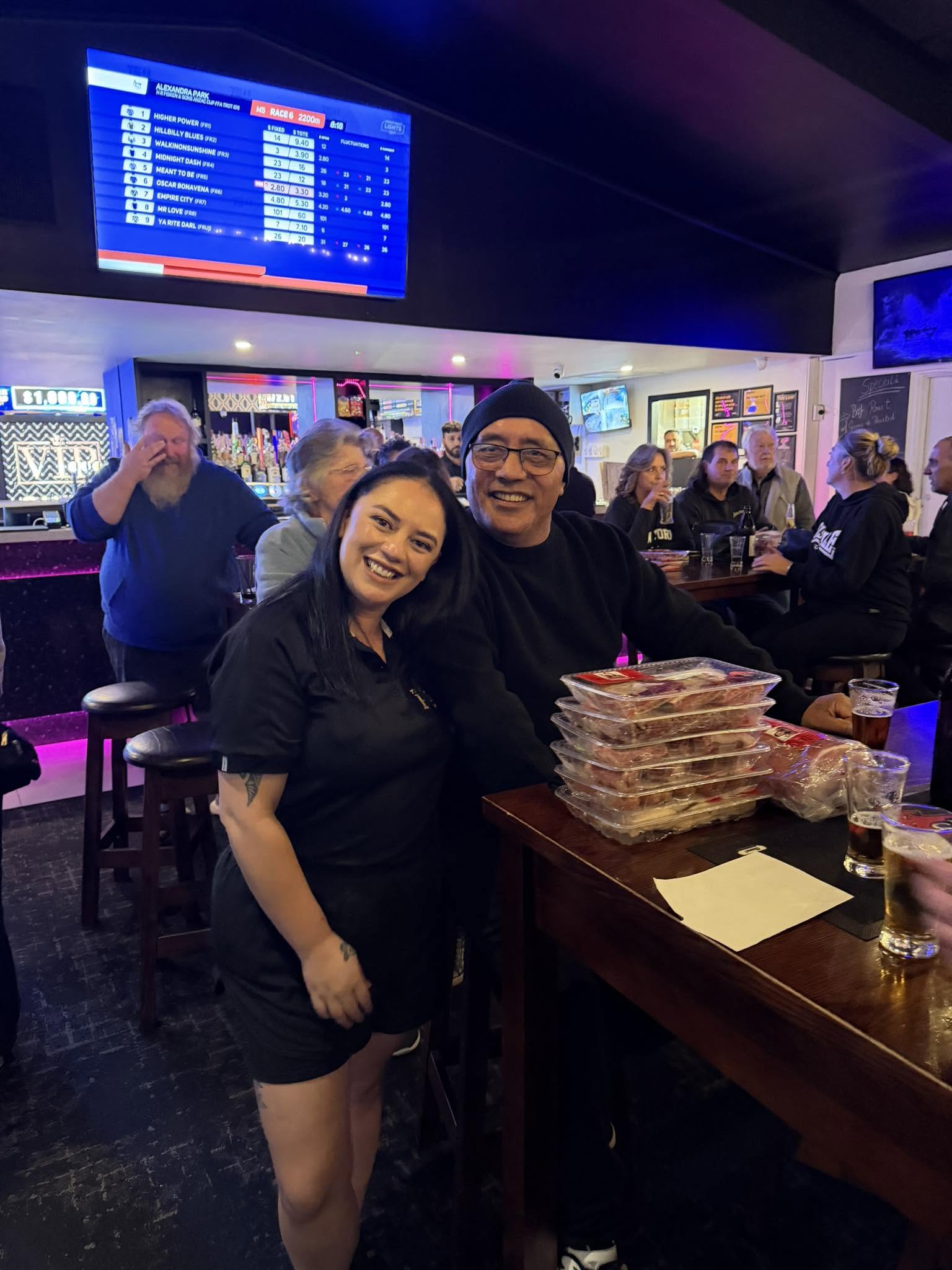 Two smiling patrons with a stack of meat trays at The Riccs